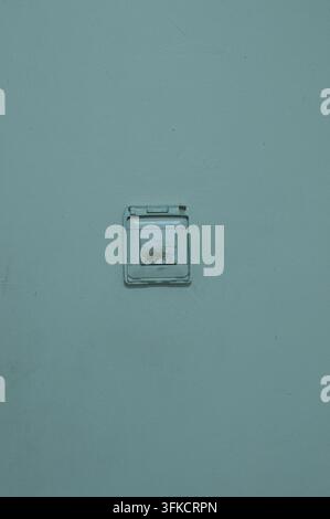 Un vieux interrupteur blanc sale monté sur un mur intérieur bleu clair, montrant des signes d'usure et d'utilisation quotidienne dans une pièce d'un bâtiment. Banque D'Images