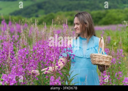 Femme calme touchant délicatement des fleurs violettes éclatantes, lumière naturelle douce, fond de collines vertes luxuriantes, profondeur de champ peu profonde, atmosphère rurale sereine Banque D'Images