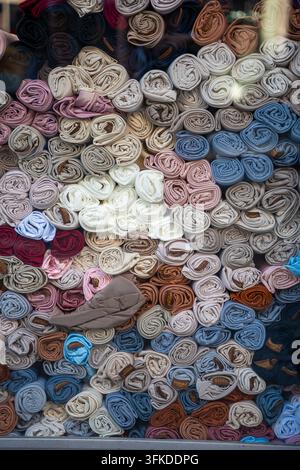 Roules de tissu colorées soigneusement disposées dans une vitrine, mettant en valeur différentes nuances et textures de textiles dans un présentoir vibrant et visuellement attrayant Banque D'Images