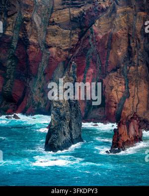 Prise verticale de falaises volcaniques dramatiques s'élevant des eaux turquoise tumultueuses de l'océan devant une toile de fond de falaises colorées, rouges et brunes en couches Banque D'Images