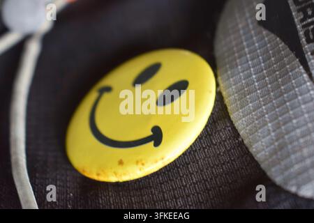Badge jaune en forme de smiley reposant sur un tissu sombre. Banque D'Images
