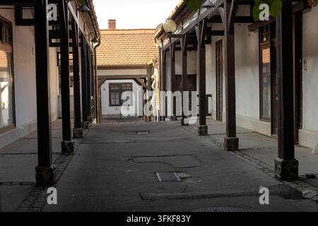 Un passage étroit de cour couvert, bordé de supports en bois, de murs en plâtre blanc, de portes et fenêtres en bois ainsi que de toits carrelés. Une lumière chaude du jour illumine Banque D'Images