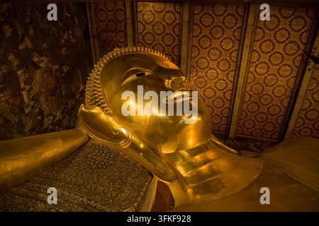 Détail rapproché de la tête dorée et du visage serein de la statue de Bouddha couché à l'intérieur du temple de Wat Pho, Thaïlande, mettant en valeur un artisanat complexe Banque D'Images