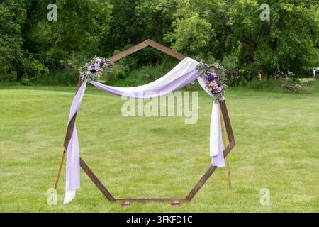 Arche de mariage en bois hexagonale décorée de tissu et de fleurs violettes dans un jardin verdoyant Banque D'Images