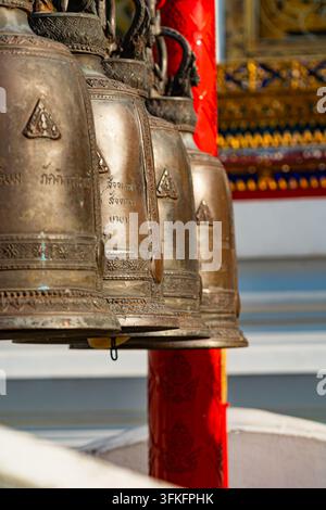 Vue en perspective d'une rangée de clochettes de prière traditionnelles en bronze avec des inscriptions thaïlandaises gravées, suspendues dans un temple à Bangkok, Thaïlande Banque D'Images