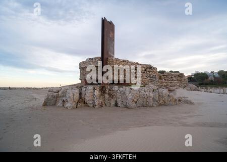 Un bunker en pierre érodé avec une structure métallique rouillée se dresse sur la plage de sable de Tarragone, en Espagne, sous un ciel nuageux. Banque D'Images