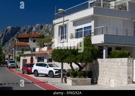 4 juillet 2026, Kotor, Monténégro, Extérieur d'une villa côtière blanche à deux étages avec des rampes de balcon en verre, des tuiles de toit en terre cuite et une limite en pierre Banque D'Images