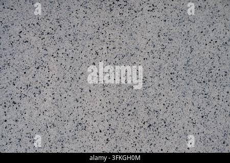 Une texture de fond uniforme et plate montrant une surface en pierre composite ou en quartz gris clair et finement grainée uniformément saupoudrée de minuscules points noirs et charc Banque D'Images