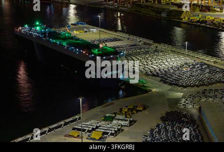 Grand navire de charge amarré à Keratsini, Attiki, Grèce, illuminé la nuit, chargeant de nouveaux véhicules et automobiles à un terminal animé, illustrant le caractère mondial Banque D'Images