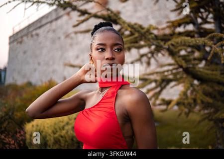 Femme élégante dans une robe rouge frappante pose gracieusement devant un magnifique arrière-plan naturel Banque D'Images