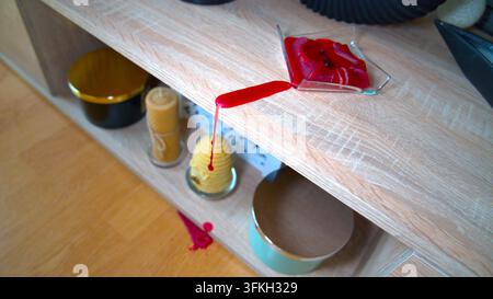 De la cire fondue rouge dégoulinant d'une étagère en bois sur le sol à l'intérieur. Banque D'Images