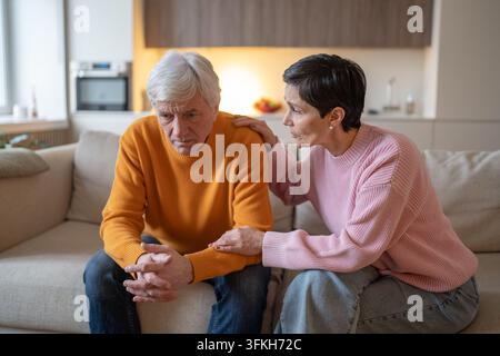 Épouse âgée attentionnée réconforte son mari en détresse alors que le couple âgé est assis ensemble sur le canapé de la maison Banque D'Images