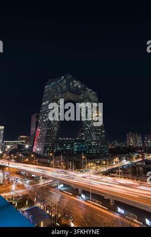 Vue nocturne du siège de CCTV à Pékin avec des traînées de lumière vibrantes provenant de la circulation routière Banque D'Images