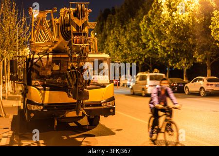 Scène de rue nocturne avec une grue et un cycliste passant à proximité Banque D'Images