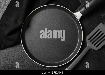 Cuisine saine et préparation de repas, poêle à crêpes antiadhésive vide avec spatule et torchon sur un fond texturé sombre pour recette culinaire Banque D'Images