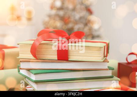 Offrandes de Noël et lecture, pile de livres enveloppés d’un ruban rouge pour un cadeau de Noël dans un intérieur festif avec des lumières floues Banque D'Images
