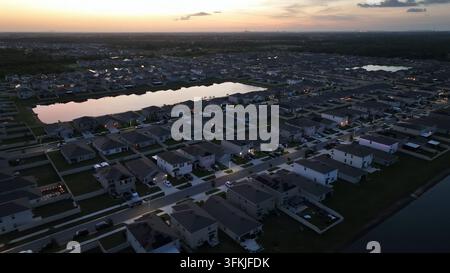 Heure dorée dans un quartier luxueux avec des manoirs et un lac privé au centre du quartier. Réflexion du soleil à l’heure du coucher. Plan latéral aérien large. Luxu Banque D'Images