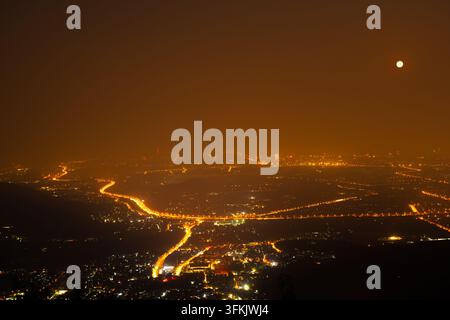 La pleine lune plane sur Fragrant Hills à Pékin, les lumières de la ville brillant d'un orange chaud à travers le paysage urbain Banque D'Images