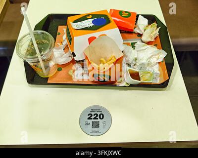 Kirov, Russie – 19 août 2026 : Une boîte à burger orange et des frites partiellement mangées sont posées parmi des restes de laitue et des mouchoirs usagés, avec le numéro de table 220 visible Banque D'Images