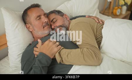 Homme d'âge moyen câlinant avec la main sur la poitrine tout en étant allongé sur un lit les yeux fermés à l'intérieur d'un bâtiment ; intimité tranquille. Banque D'Images