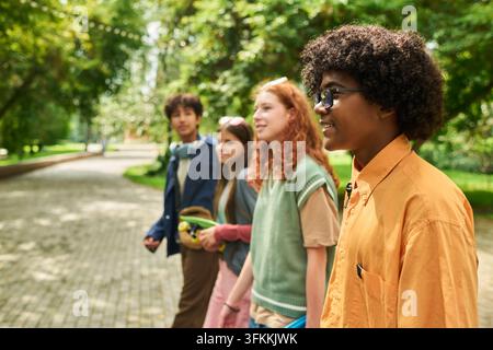 Groupe divers d'adolescents souriants marchant ensemble dans un parc en été Banque D'Images