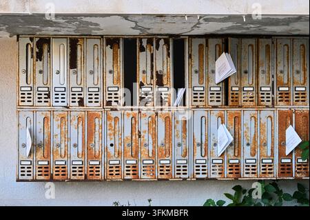 Photographie détaillée horizontale d'un grand bloc de boîtes aux lettres métalliques vieilles, usées et rouillées avec du courrier papier et des prospectus qui dépassent Banque D'Images