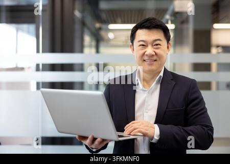 Homme d'affaires utilisant un ordinateur portable pour l'analyse financière et la communication d'entreprise dans un bureau moderne. Professionnel souriant travaillant sur un ordinateur pour stimuler la croissance et le développement stratégique de l'entreprise. Banque D'Images