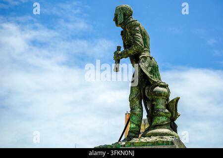 Statue en bronze patiné vert usé d'un officier de marine tenant un télescope, montée sur un piédestal orné contre un ciel bleu. Banque D'Images