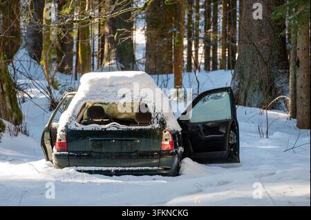 Voiture verte foncée abandonnée partiellement ensevelie dans une congère, couverte de neige sur le toit et avec une porte ouverte, créant une scène hivernale frappante. Banque D'Images