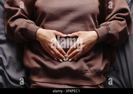 Femme enceinte faisant une forme de cœur avec ses mains sur le ventre. Fond de grossesse pour la maternité, bébé attendu, maternité, amour et famille. Banque D'Images