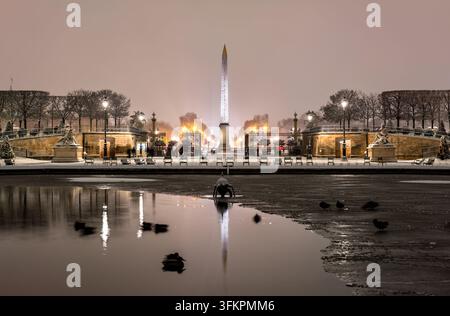 Obélisque de Louxor illuminé à la Place de la Concorde vu depuis le jardin des Tuileries enneigé la nuit à Paris, France. Banque D'Images