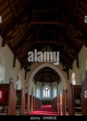 20 septembre 2026, Loweswater, Royaume-Uni. La lumière du soleil traverse les fenêtres cintrées d'une église historique, illuminant l'allée recouverte d'un tapis rouge Banque D'Images