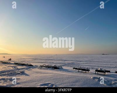 Coucher de soleil d'hiver sur un lac gelé avec des chaises de plage vides Banque D'Images