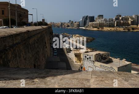 Une image amusante montrant un chat d'art mural dépassant les murs de la ville de La Valette avec Sliema en arrière-plan. Banque D'Images