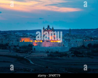 Vue aérienne de la ville fortifiée historique de Mdina au crépuscule, mettant en vedette la cathédrale Saint-Paul illuminée et les anciens murs de pierre à Mdina, ouest Banque D'Images