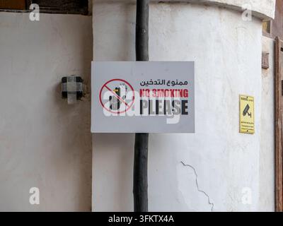 Panneau bilingue d'interdiction de fumer en arabe et en anglais monté sur un poteau devant un mur en plâtre texturé à Souq Waqif. Banque D'Images