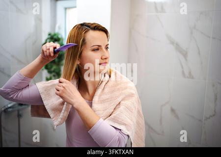 Femme peignant ses cheveux blonds mouillés dans la salle de bain après la douche Banque D'Images