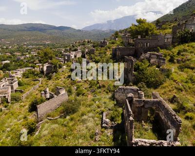Vue aérienne des ruines historiques en pierre du village fantôme de Kayakoy entouré de végétation luxuriante et de montagnes à Fethiye, Mugla, Turkiye. Banque D'Images
