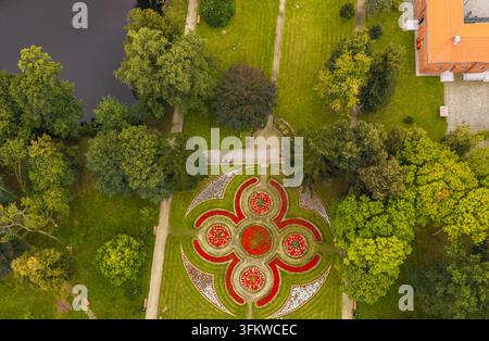 Vue aérienne d'un parterre de fleurs géométrique dans le parc du Palais des Évêques, entouré d'arbres luxuriants, d'un étang et d'un bâtiment en briques à Pelplin, en Poméranie Banque D'Images