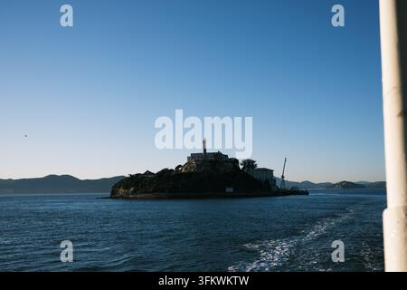Île d'Alcatraz depuis un ferry en départ dans une lumière dorée. L'île brille d'une lumière chaude alors que le bateau s'éloigne. Banque D'Images