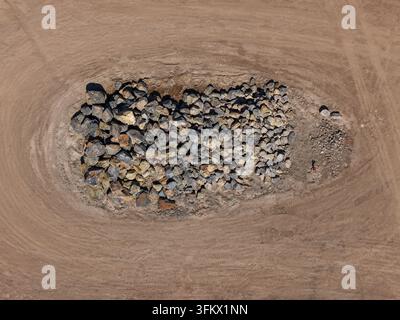 Vue aérienne d'un grand tas de roches et de blocs situés au centre d'un champ de terre défriché avec des traces de pneus visibles à Kilsyth, Victoria, Austra Banque D'Images