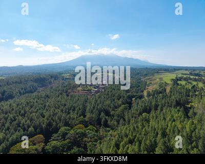 Cette vue aérienne époustouflante capture une vaste forêt verte au premier plan avec le majestueux mont Kawi au loin à Ngajum, Malang Banque D'Images