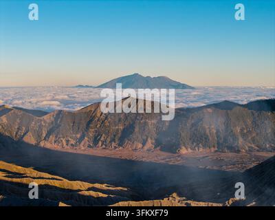 Les montagnes s'élèvent au-dessus d'une mer de nuages. La lumière du soleil brille chaleureusement sur les pics déchiquetés au-dessus de la mer de sable de Bromo Banque D'Images