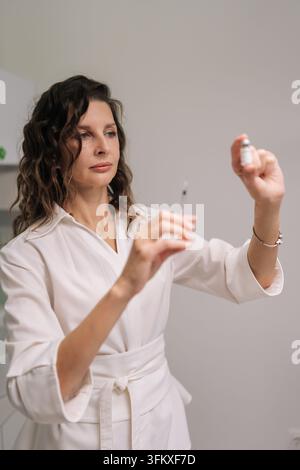 Portrait d'un professionnel médical remplissant une seringue avec un médicament provenant d'une fiole, préparant pour une procédure esthétique dans une clinique de médecine esthétique. Concept de Banque D'Images
