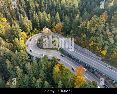 Vue aérienne d'une courbe de route de montagne en épingle à cheveux avec une croix sur rocher en automne Banque D'Images