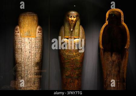 COPENHAGUE, DANEMARK - 25 AOÛT 2025 : Trois sarcophages égyptiens anciens richement décorés exposés dans une galerie muséale faiblement éclairée, montrant des hiéroglyphes Banque D'Images