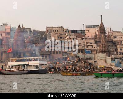 VARANASI, INDE - 23 JANVIER 2026 : Des bateaux se rassemblent près des lieux de crémation alors que les bûchers funéraires brûlent le long des rives du Gange. Banque D'Images