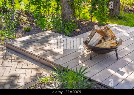 Une terrasse de jardin sereine avec une terrasse en bois et un bol à feu en métal Banque D'Images