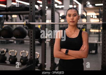 Un plan moyen professionnel d'une jeune femme thaïe Isan asiatique confiante, debout les bras croisés et regardant directement la caméra dans un moderne Banque D'Images
