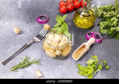 Champignons bien entretenus dans un bocal en verre. Accompagnés de feuilles de basilic frais. Tomates cerises. Huile d'olive. Gousses d'ail. Rondelles d'oignon rouge. Persil. Romarin Banque D'Images